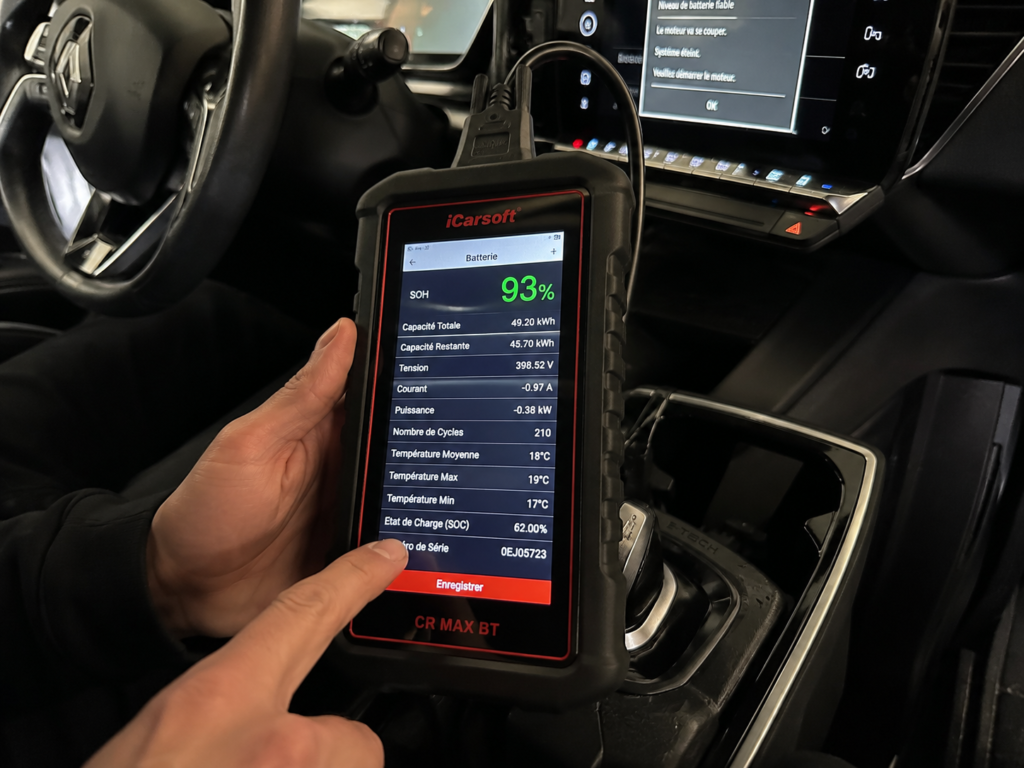 Technicien réalisant un diagnostic du SOH d'une batterie de voiture électrique avec un appareil OBD branché dans l'habitacle.